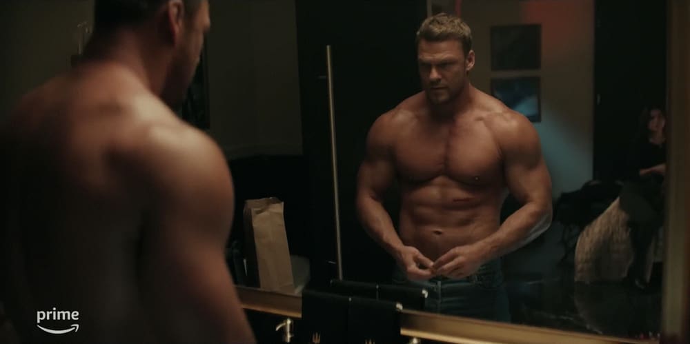 A shirtless Alan Ritchson looks at himself in a mirror in 'Reacher'.